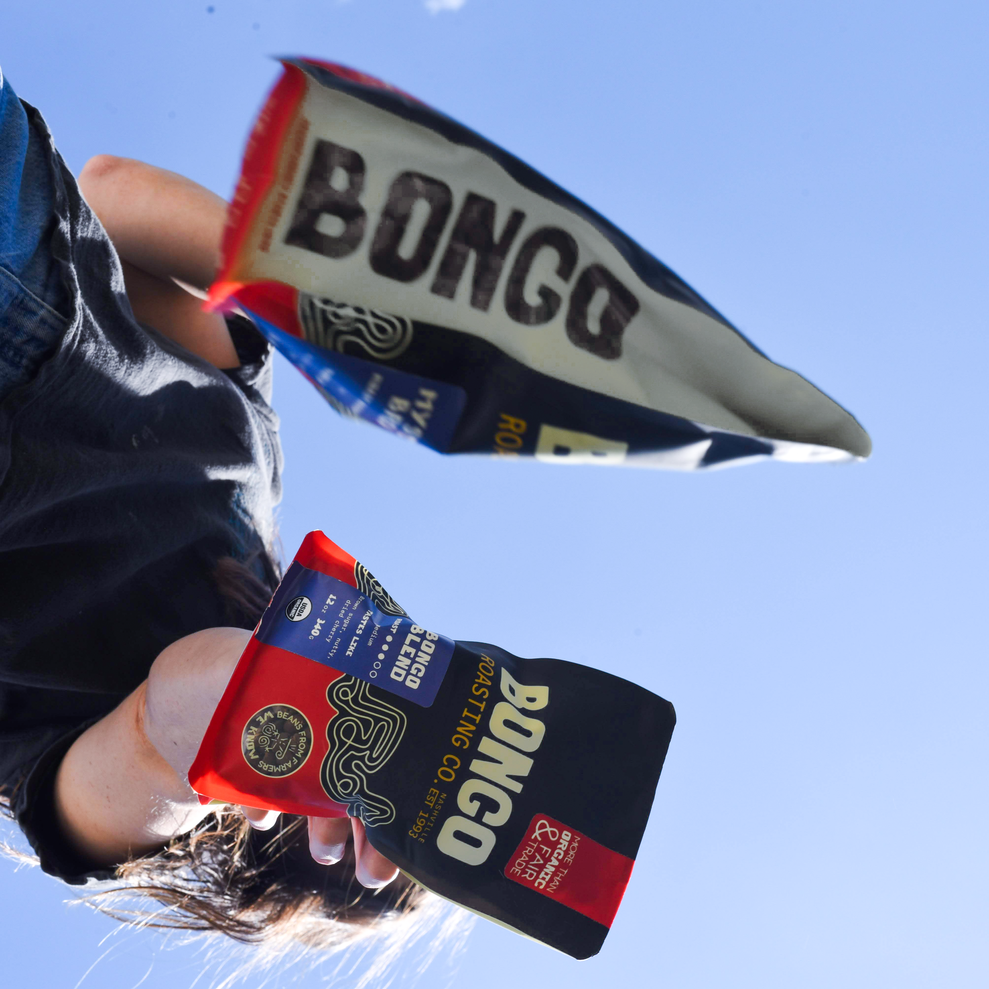 Person holding Bongo brand coffee bags against a clear blue sky