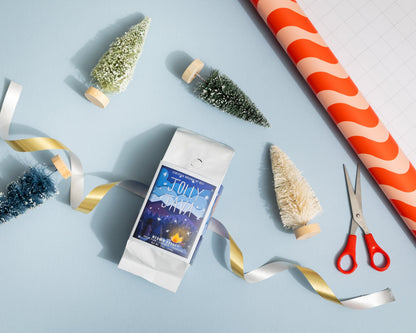 Festive scene with Jolly coffee package, decorative trees, ribbons, and scissors on a light blue background